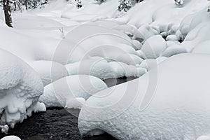 Powder snowdrifts on the stones of mountain river and forest snowfall