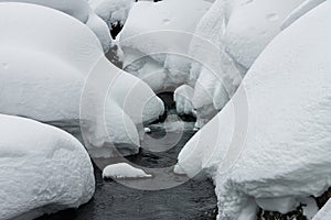 Powder snowdrifts on the stones of mountain river and forest snowfall