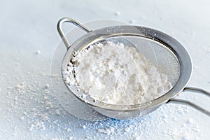 Powdered Confectioners Sugar in Sieve Closeup over Pastel Blue