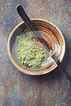 Powdered matcha green tea and chashaku matcha spoon on rustic stone background.