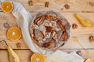 A powdered pear pie decorated with white cloth, fresh sliced pears, dried oranges, walnuts, anise stars, spoon on the wooden table