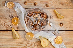 A powdered pear pie decorated with white cloth, fresh sliced pears, dried oranges, walnuts and silver spoon on the wooden board