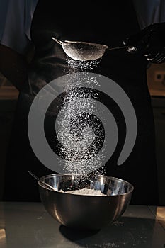powdered sugar or flour is sifted into a bowl on a black background.