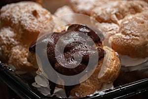 Powdered sugar and shiny chocolate glased puffs filled with a swirl of white whipped cream