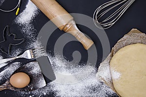 Powdering by flour rolled out dough for bakary stics with wooden rolling pin over black basground.