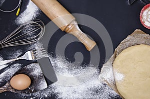 Powdering by flour rolled out dough for bakary stics with wooden rolling pin over black basground.