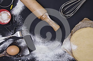 Powdering by flour rolled out dough for bakary stics with wooden rolling pin over black basground.