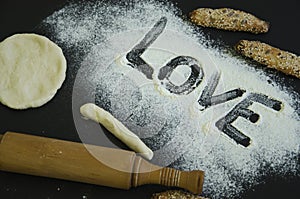 Powdering by flour rolled out dough for bakary stics with wooden rolling pin over black basground. With love