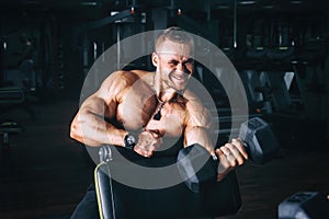 Power athletic guy bodybuilder, execute exercise with dumbbells, in dark gym