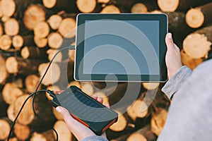 Power Bank in the girl`s hand, on the background of a tablet and a round tree