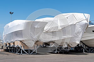 Power boat parked covered white protective plastic film New boats in cover casing shrink wrap on sailboat stored for winter