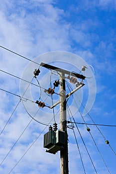 High voltage electrical power cables and transformer seen erected on a wooden pole.