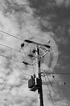 High voltage electrical power cables and transformer seen erected on a wooden pole.