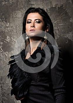 The power and confidence. Portrait of young beautiful woman with dark hair. Dress and earring with feathers