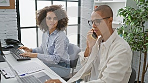 Power couple at work, two focused office workers, man and woman, skillfully multi-tasking with computer and smartphone indoors