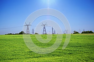 Power electric towers in a field with green grass, blue sky in the background and bright sunlight