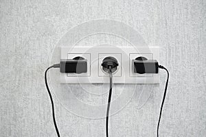 Power European electric plug  on a white. black electric cord plugged into a white electricity socket on white background