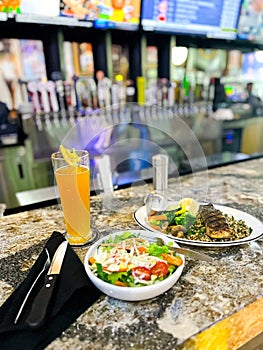 Power grain grilled salmon dish, healthy salad bowl, tall pilsner beer glass, silverware on cloth napkins, blurry beer taps, wall