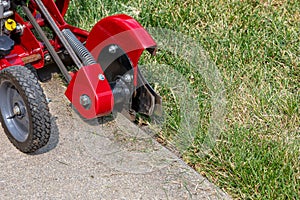 Power lawn edger trimming grass along sidewalk.