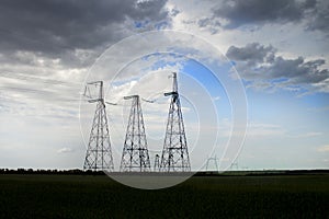 A power line in a field against a cloudy sky with clouds approaching. Power transmission poles high voltage lines on a cloudy day