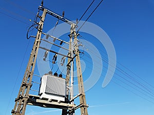 Power line post against a blue sky with a trace from a jet aircraft. Concrete construction with metal wires. Transmission of elect