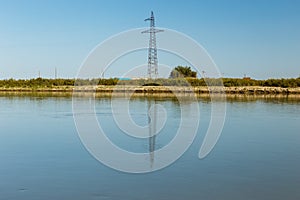 Power line pylon stands on the banks of the Syr Darya river, reflected in the water