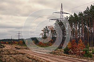 Power line tower along the dirt road near the autumn forest. Cloudy day