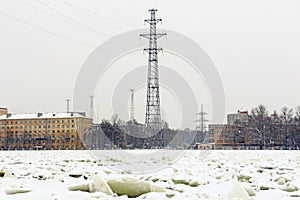 A power line tower on the bank of a frozen river