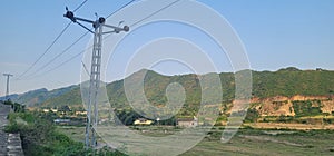 power lines above grassy field and rocky hillsides in a hilly area