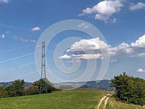 Power lines across mountains landscape, blue sky, green fields and path. Energy industry. Copy space