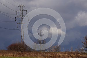 Power lines in the field against the background of a bright sky with dark snow clouds and highlighted by contrasting light from