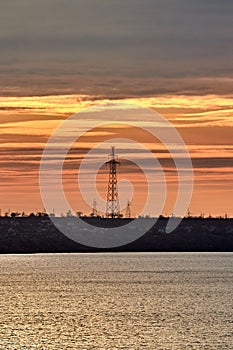 Power lines on an island in the sea against the backdrop of a yellow-orange multicolored sunset