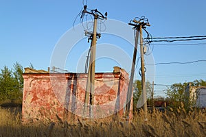 Power lines and an old building among the reeds in the rays of the sun at sunset