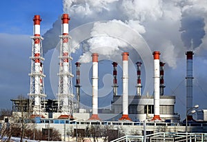 Power plant building with many high red and white industrial pipes with dense smoke