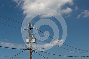 Power pole and lines with transformers and street light, blue sky with clouds