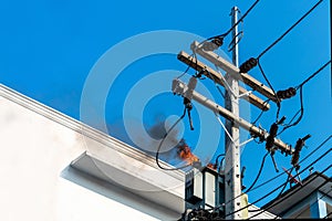 Power pylon overload or electric short circuit at transformer on poles and fire or flame with smoke on blue sky