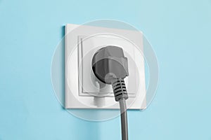 Power socket with inserted plug on light blue wall, closeup. Electrical supply