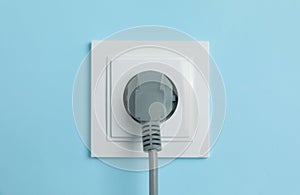 Power socket with inserted plug on light blue wall, closeup. Electrical supply