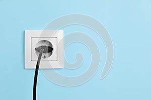 Power socket with inserted plug on light blue wall, space for text. Electrical supply