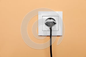 Power socket with inserted plug on pale orange wall. Electrical supply