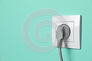 Power socket with inserted plug on turquoise wall, space for text. Electrical supply