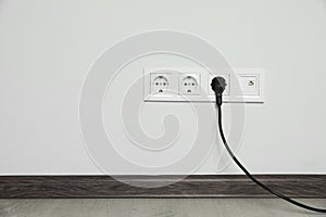 Power sockets with inserted plug on white wall indoors, space for text. Electrical supply