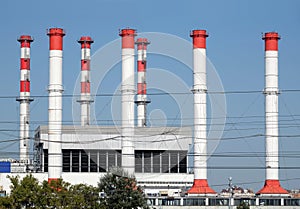 Power station building with many high red and white industrial pipes over clear cloudless blue sky