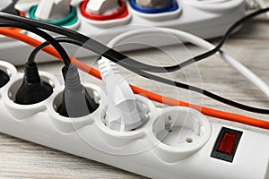 Power strip with extension cords on white wooden floor, closeup. Electrician\'s equipment