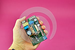 Power supply Board on pink background, top view. A person holds a printed circuit Board PCB with capacitors and diodes.