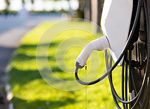 Power supply for electric car charging. Electric car charging station. Close up of the power supply plugged. Green grass blur