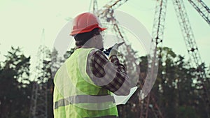 Power systems engineer on site. An engineer worker is talking on a mobile phone and checking the data in documents