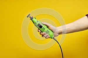Power tool. Green Die grinder in hands isolated on yellow background