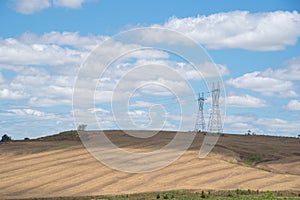Power transmission towers in an agricultural production field and the blue horizon in the background