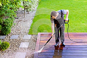 power washing - man cleaning terrace with a power washer - high water pressure cleaner on wooden terrace surface